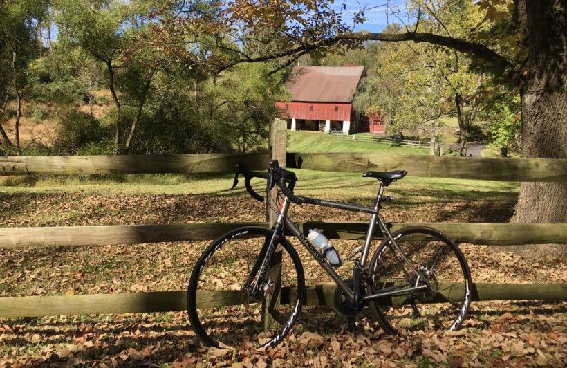 A bike leaning against a fence with a red barn in the background.