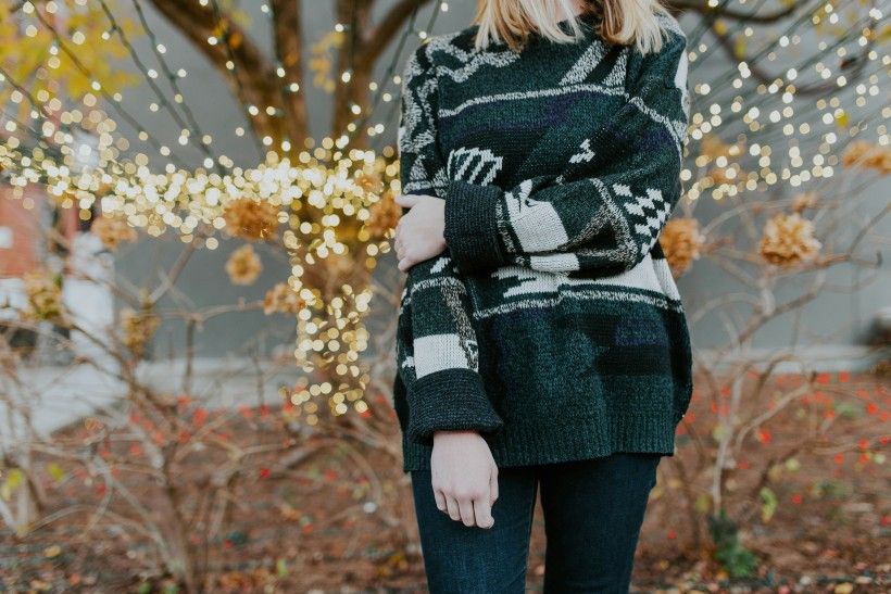 Photo credit: Brooke Cagle photo of a woman standing with arm folded wearing a sweater in front of a tree wrapped in holiday lights