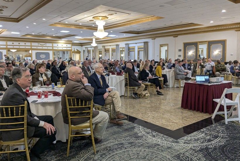 Photo of more than 100 people seated at round tables inside at a conference