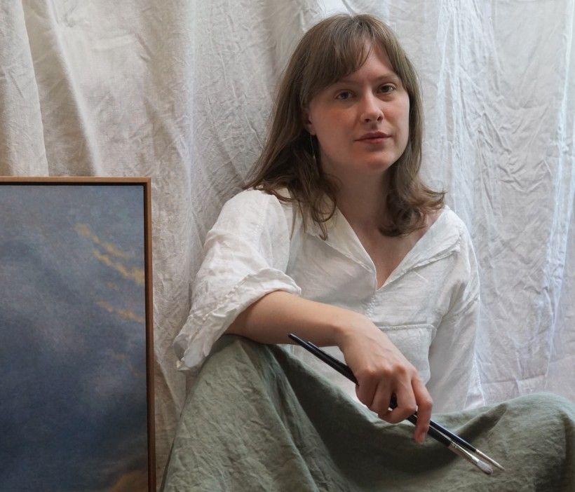 Photo of a woman holding paint brushes, seated on the floor