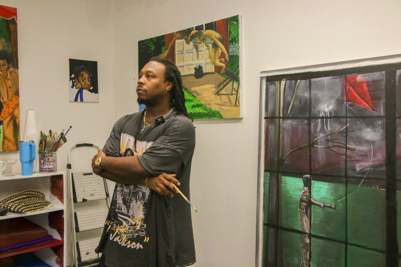 A man who is standing in front of his painting, holding a paint brush