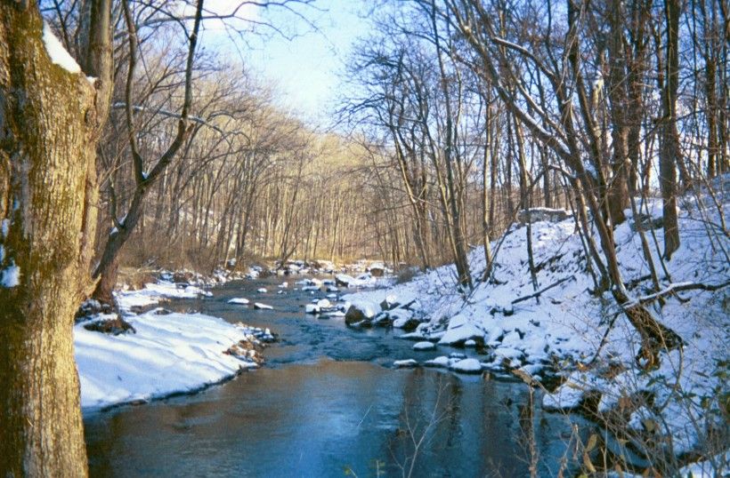 River surrounded by snow covered hills and bare trees. 