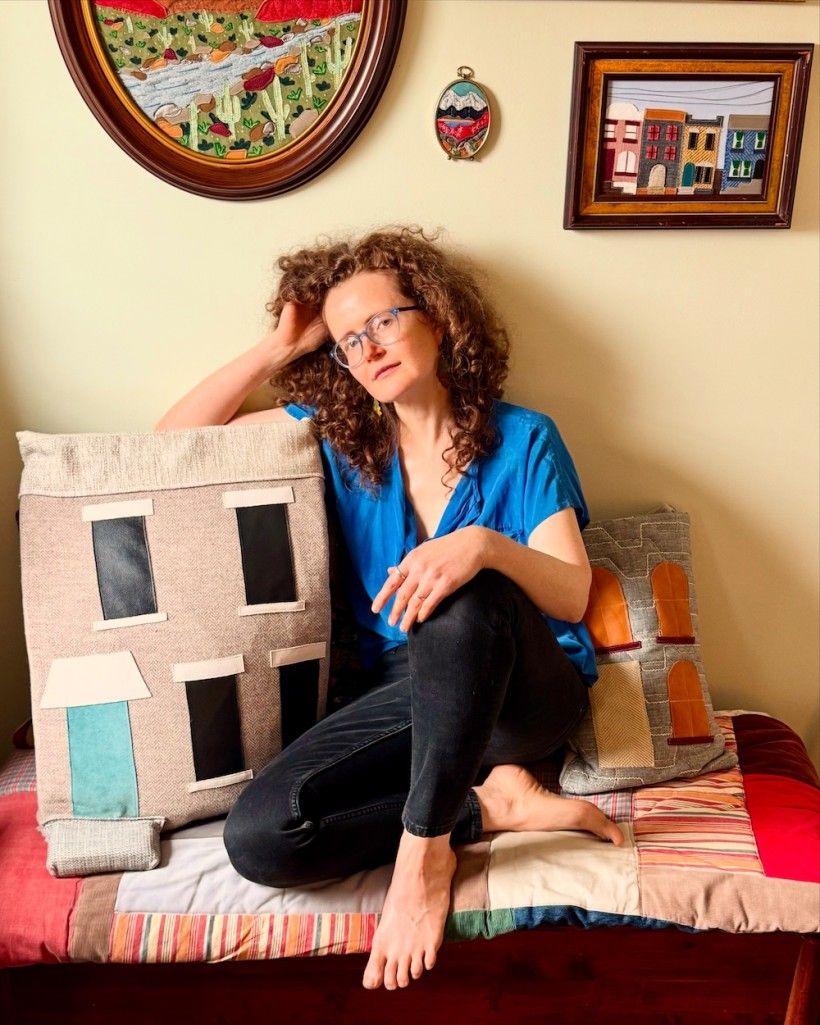 photos of a woman sitting on a colorful bench. She has red hair, glasses and is wearing a blue shirt. 