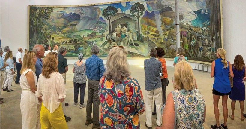 A group of people seen from behind, looking at a large Mural by N.C. Wyeth.