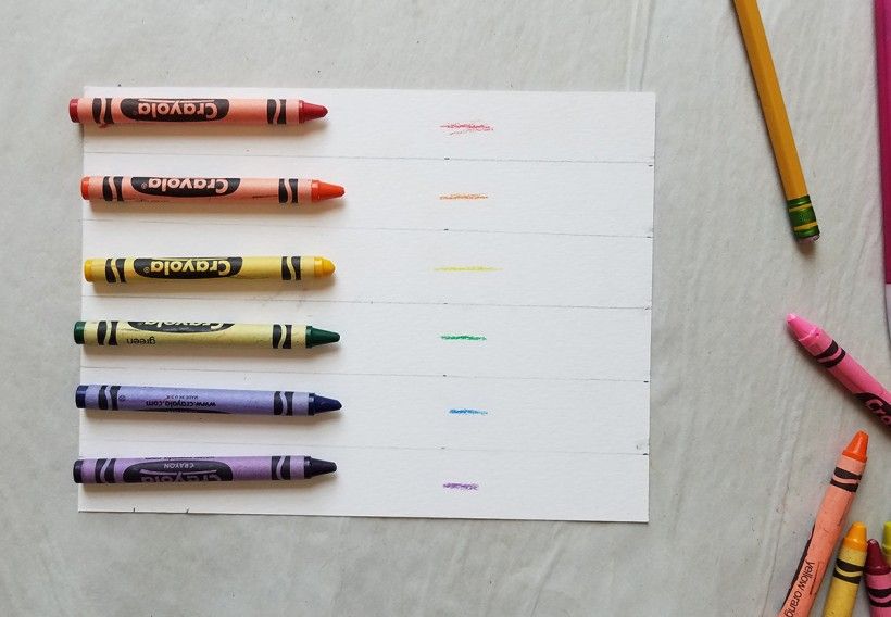 An assortment of colored crayons on top of a white piece of paper with horizontal lines