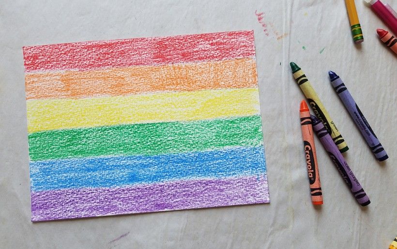 Crayons next to a piece of paper with rainbow-colored horizontal lines 