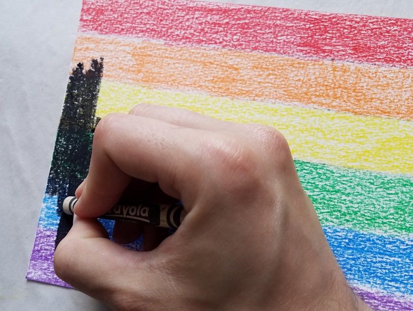 A black crayon drawing over rainbow-colored horizontal lines 