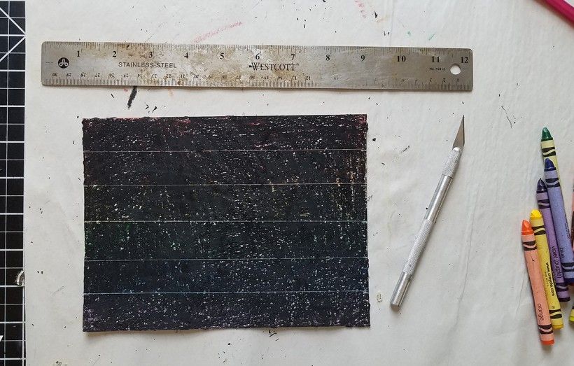 A piece of paper colored over with black crayon, next to a ruler and crayons