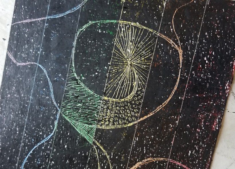 A piece of paper colored over with black crayon, with a colorful rainbow design scratched through the middle of the paper