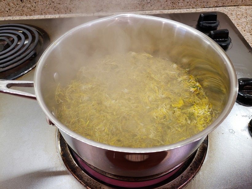 Dandelion flowers cooking in a pot with steam