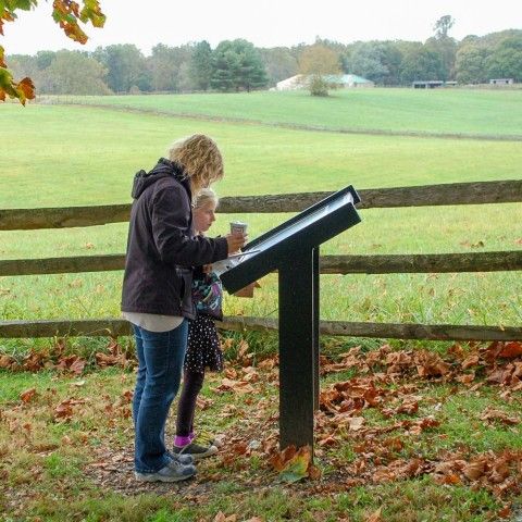 An adult and child looking at an interpretive sign with a fenced meadow in the background.