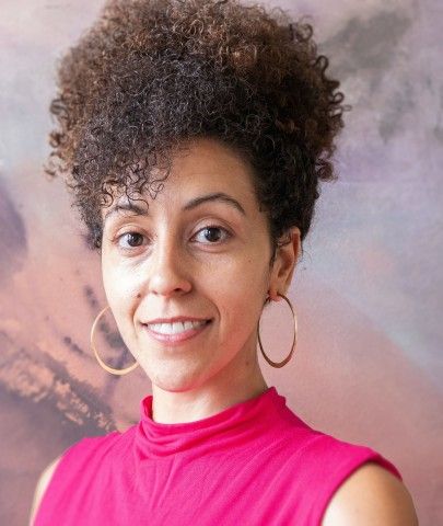 Woman in a bright pink top, wearing hoop earrings, smiling for a photo