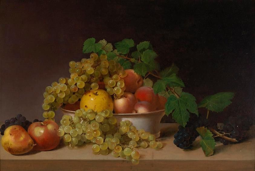 A still life painting featuring a bowl of fruit, including yellow grapes cascading over the edge, a central yellow pear, and several peaches. Dark grapes and green leaves are scattered around the wooden table against a dark background.
