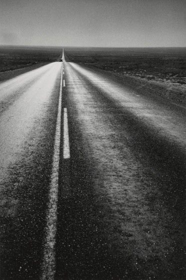 A black and white shot of an open road from the perspective of the center of the road that goes on for miles.